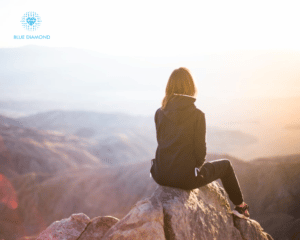 woman looking out at scenery on top of a mountain with blue diamond logo