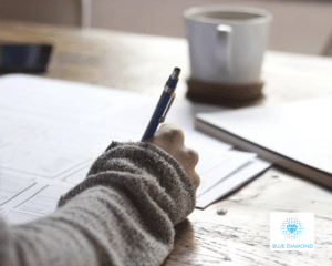 girl writing and planning on paper in office with mug and blue diamond logo